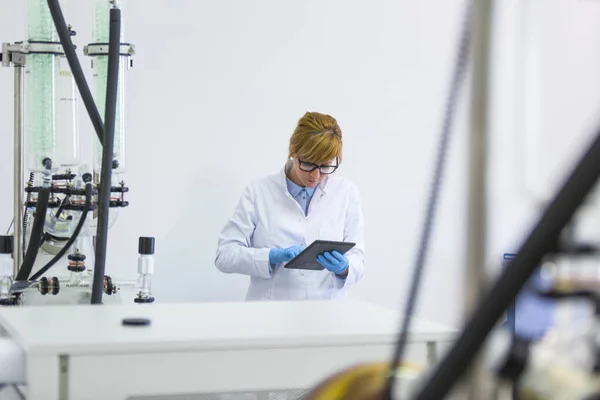 stock image Scientist typing on black tablet in laboratory during CBDa oil extraction. She is wearing rubber gloves and stands next to rotational vaporizer with green condenser called rotavapor.