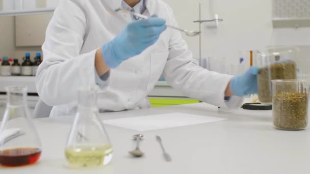 科学者は実験室の白い紙にマリファナの種を選ぶ Cbd油を含むガラス管が背景にあります 健康コンセプト — ストック動画