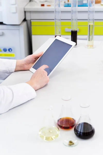 Hands using tablet over laboratory desk. Hemp seeds, marijuana bud, CBD and CBDa oils are on table. Cannabis pharmaceutical healthcare concept.