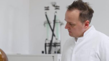 Bilim adamı CBD yağ çıkarma sırasında laboratuvarda rotovapor inceliyor. Lastik eldiven takıyor ve yeşil yoğunlaştırıcılı döner buharlaştırıcının yanında duruyor..