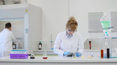 Laboratuvarda kenevir CBD, CBDA yağları ve tabletle çalışan iki bilim adamı. Lateks eldiven, cam tüpler ve erlenmeyer şişeleri kullanıyorlar. Esrar tohumlarından alınan sağlık hizmetleri eczanesi.
