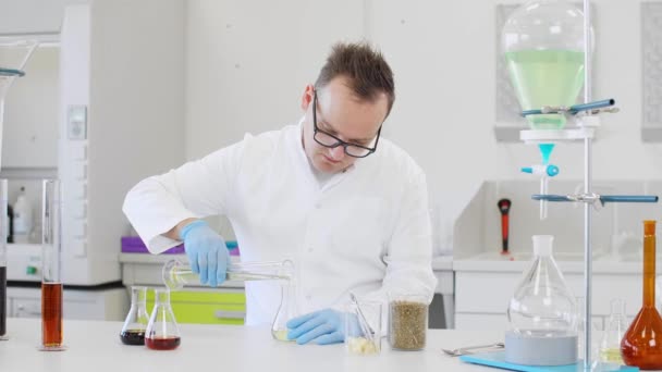 実験室で大麻CbdやCbdaの油で働く眼鏡をかけている男性化学者 彼はラテックス手袋 ガラス管とエルレンマイヤーフラスコを使用しています 大麻の種からの医療薬局 — ストック動画