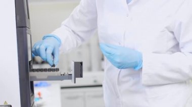 Gözlük ve lastik eldiven takan kadın kimya bilimci ilaç laboratuvar deneyi sırasında kromatografi makinesindeki küçük bir delikten CBD yağı örnekleri alıyor. Esrardan elde edilen sağlık hizmetleri.