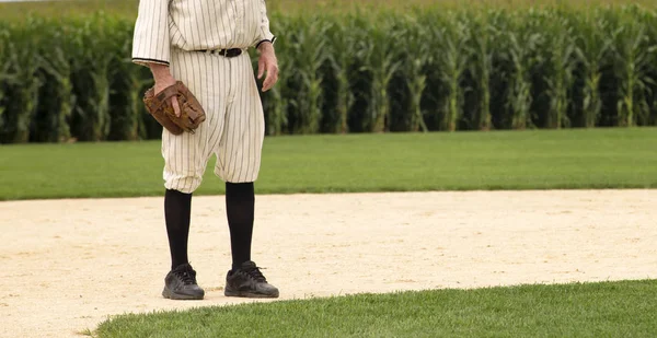 Baseball player in old baseball uniform and baseball glove, on the playing field.  Corn in the background.  Field of Dreams  