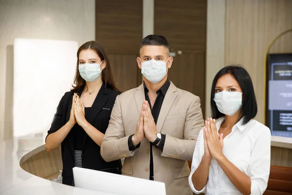 hotel receptionist wearing mask to protect from conronavirus covid 19 having new practice of greeting with thai wai, new greeting practice in coronavirus covid 19 pandemic