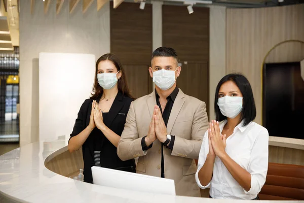 hotel receptionist wearing mask to protect from conronavirus covid 19 having new practice of greeting with thai wai, new greeting practice in coronavirus covid 19 pandemic