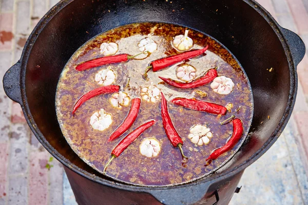 National Uzbek dish pilaf, pilaw, plov, rice with meat in big pan. Cooking process in a cauldron on fire.  Preparation stages. pour out rice, Add waters, red pepper and the whole garlic — Stock Photo, Image