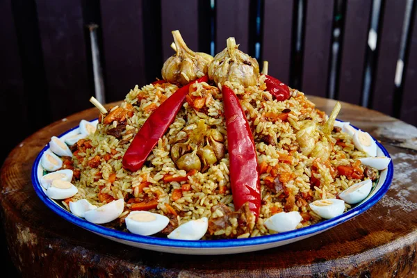 Nationale Oezbeekse schotel pilaf. Koken in een ketel in brand. Verspreid prachtig op een nationale plaat lyagan rijst, van boven plakjes van het uitgesneden vlees en versieren met rode peper en knoflook — Stockfoto