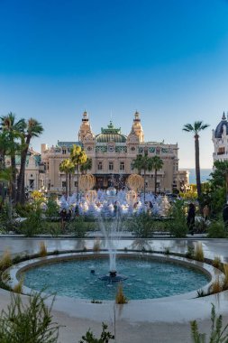 Monaco, Monte-Carlo, 25 Aralık 2019: Günbatımında Monte-Carlo Meydanı, beyaz Noel ağaçları, Paris Oteli, güneşli gün, Noel süsü, turistler, çeşme, yeni evler, yeşil çimenler