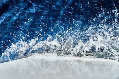 Yelkenli beyaz bir teknenin burnu suyu keser, püskürtür, güneş ışığında su parlar.