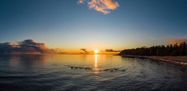 Dronlar gün batımında kıyıda uçuyor, pitoresk günbatımı, sessiz bir su, kumlu bir sahil, ağaçların tepeleri günbatımı güneşiyle aydınlanıyor, pembe bulutlar.