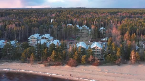 Techos de casas en el bosque, la pintoresca costa al atardecer, aguas tranquilas, copas de árboles iluminadas por el sol al atardecer, nubes rosadas — Vídeo de stock