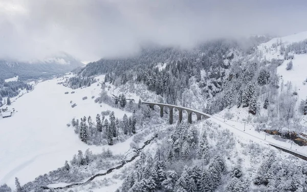 Vista aérea del viaducto de Landwasser con ferrocarril sin tren famoso en invierno, hito de Suiza, nevando, río y montañas — Foto de Stock