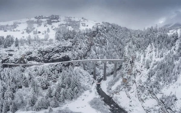 Vista aérea del viaducto de Landwasser con ferrocarril sin tren famoso en invierno, hito de Suiza, nevando, río y montañas — Foto de Stock