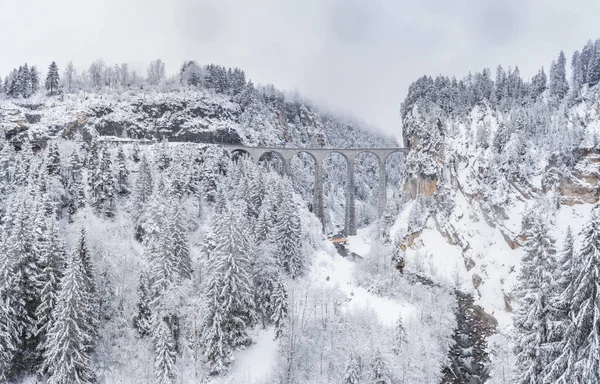 Vista aérea del viaducto de Landwasser con ferrocarril sin tren famoso en invierno, hito de Suiza, nevando, río y montañas — Foto de Stock