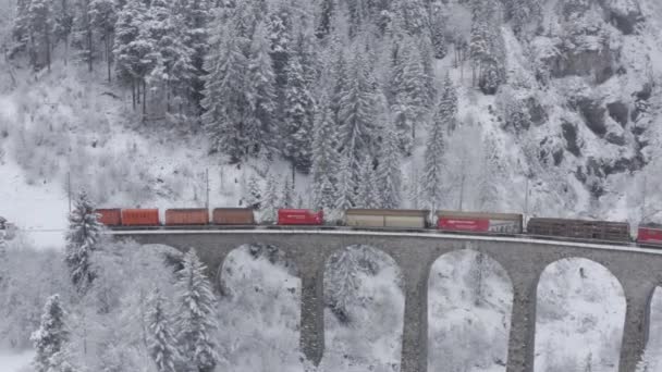 Aerial View of the Landwasser Viaduct a tehervonat piros színű télen, mérföldkő Svájc, havazás, drón fordul vonatok után — Stock videók