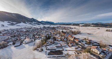 Kış mevsiminde gün doğumunda dağın dibindeki küçük Alman kasabasının hava manzarası Halblech şehri, Almanya, Bavyera, ağaçların dalları kıpkırmızı, güneşli havayla kaplıdır.