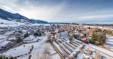 Kış mevsiminde gün doğumunda dağın dibindeki küçük Alman kasabasının hava manzarası Halblech şehri, Almanya, Bavyera, ağaçların dalları kıpkırmızı, güneşli havayla kaplıdır.