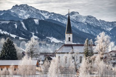 Kış mevsiminde gün doğumunda dağın dibindeki küçük Alman kasabasının hava manzarası Halblech şehri, Almanya, Bavyera, ağaçların dalları kıpkırmızı, güneşli havayla kaplıdır.