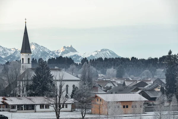 Luftaufnahme der kleinen gemütlichen deutschen Stadt am Fuße des Berges bei Sonnenaufgang in einer Wintersaison, Halblech Stadt, Deutschland, Bayern, Zweige der Bäume sind mit Raureif bedeckt, sonniges Wetter — Stockfoto