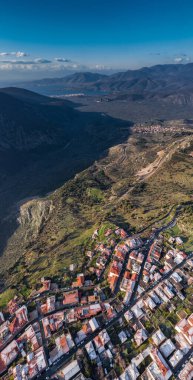 Gündoğumunda Delphi, Yunanistan 'ın havadan görünüşü, Korint Körfezi, Dağların üzerinde sabah sisi, çatılarda karlar, ön planda çatıları olan katmanlı tepeler.