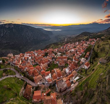 Delphi, Yunanistan, Korint Körfezi 'nin havadan görünüşü, turuncu bulutlar, katmanlı tepeler ve ön planda çatılar.