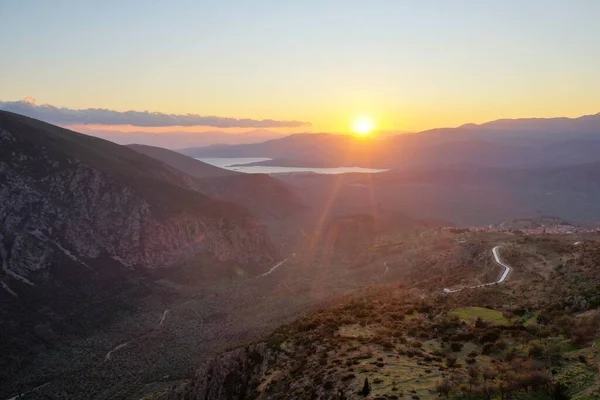 Vue aérienne de Delphes, Grèce, le golfe de Corinthe, couleur orange des nuages, flanc de montagne avec des collines stratifiées au-delà avec des toits au premier plan — Photo