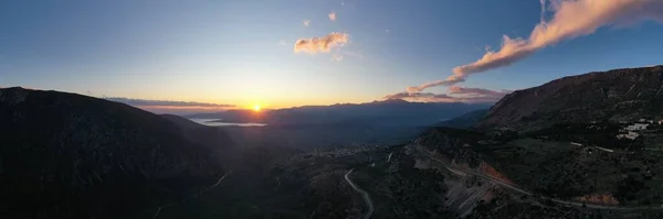 Vue aérienne de Delphes, Grèce, le golfe de Corinthe, couleur orange des nuages, flanc de montagne avec des collines stratifiées au-delà avec des toits au premier plan — Photo