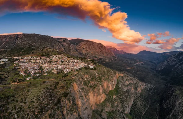 Delphi, Yunanistan, Korint Körfezi 'nin havadan görünüşü, turuncu bulutlar, katmanlı tepeler ve ön planda çatılar.