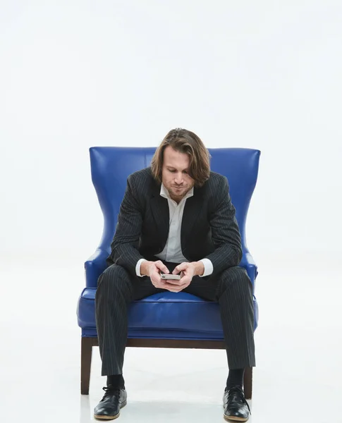 Los hombres guapos en traje negro se sienta en una silla azul, él es triste, hombre brutal con pelos largos, camisa blanca, hombre de negocios, muy elegante, mirando en el teléfono inteligente —  Fotos de Stock
