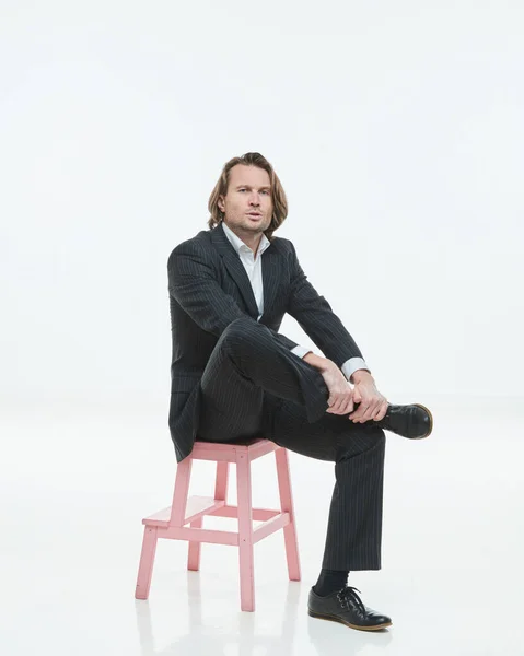 Os homens bonitos de terno preto se senta em uma cadeira rosa, homem brutal com cabelos longos, camisa branca, homem de negócios, muito elegante, olhando para a câmera — Fotografia de Stock
