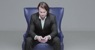 Siyah takım elbiseli yakışıklı genç adam koltukta, seviniyor, borsa oyunu oynuyor, takasların düşüşü, uzun saçlı vahşi adam, beyaz gömlek, iş adamı, çok şık, çok mutlu.