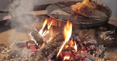 Turşulu etin büyük bir parçası yuvarlak bir ızgarada, büyük çıplak ateşin yanında, et turşusu hardal, kırmızı kömür, duman, odun, aşçının elleri kömür, ultra HD kalitesinde, 4k video kalitesinde.