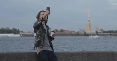 Yakışıklı adamlar birini bekliyor, kahve içiyor ve telefona bakıyor, asker ceketi ve kot pantolon giyiyor, Peter ve Paul kalesi arka planda.