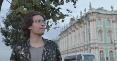 Yakışıklı adam birini bekliyor, kahve içiyor ve telefona bakıyor, askeri ceket ve kot giyiyor, devlet münzevi müzesi arka planda.