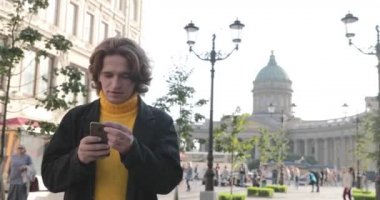 Yakışıklı adamlar birini bekliyor, sarı kazak ve siyah yağmurluk giymiş, Bolshaya Konyushennaya caddesi ve Kazan Katedrali, güneşli bir gün.