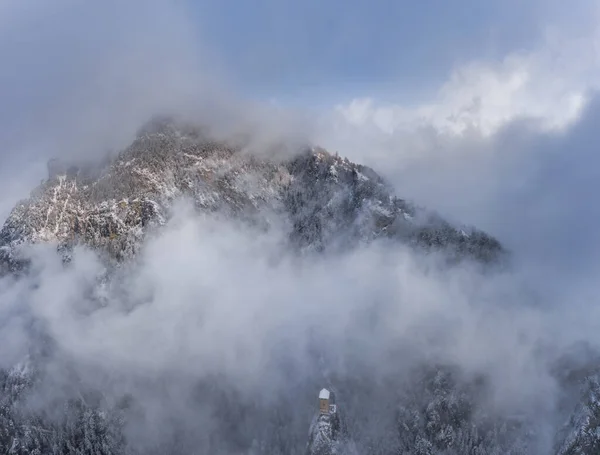 Vista aérea de la montaña con torre de límite, bosque debajo de la niebla, pendientes con nieve cubierta en Suiza, ambiente nublado, hermosas condiciones — Foto de Stock