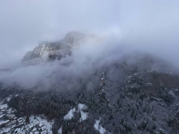 Vista aérea de la montaña con torre de límite, bosque debajo de la niebla, pendientes con nieve cubierta en Suiza, ambiente nublado, hermosas condiciones — Foto de Stock