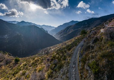 Bulutlar ve sis, köprü ve viyadük, yol boyunca dağ nehri ve arka planda karla kaplı dağlarla kaplı güzel manzaralı bir otobanın havadan panoramik görüntüsü.