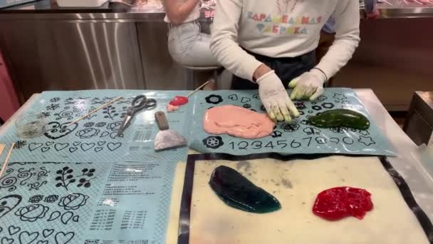 รัสเซีย เซนต์ปีเตอร์สเบิร์ก 27 มีนาคม ค.ศ. 2020: ชายหนุ่มปั้นมือจากขนมคาราเมลเหลวบนไม้ ลูกอมสีเขียวและสีแดง มือในถุงมือ — วีดีโอสต็อก