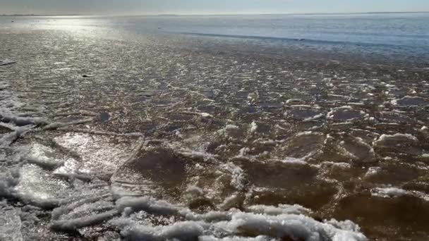 Delar av is flyter på vågor, istavlor, sandig kust, stenar, vårlandskap, soligt väder, pacificering — Stockvideo