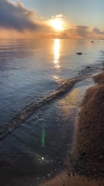 A costa no pôr-do-sol, o pôr-do-sol pitoresco, a água tranquila, uma praia arenosa, as nuvens iluminam-se pelo sol de pôr-do-sol, reflexão especular na água — Vídeo de Stock