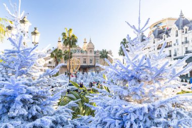 Monaco, Monte-Carlo, 25 Aralık 2019: Günbatımında Monte-Carlo Meydanı, beyaz Noel ağaçları, Paris Oteli, güneşli gün, Noel süsü, turistler, çeşme, yeni evler, yeşil çimenler