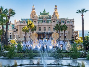 Monaco, Monte-Carlo, 25 Aralık 2019: Günbatımında Monte-Carlo Meydanı, beyaz Noel ağaçları, Paris Oteli, güneşli gün, Noel süsü, turistler, çeşme, yeni evler, yeşil çimenler