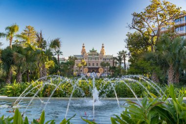 Monaco, Monte-Carlo, 25 Aralık 2019: Günbatımında Monte-Carlo Meydanı, beyaz Noel ağaçları, Paris Oteli, güneşli gün, Noel süsü, turistler, çeşme, yeni evler, yeşil çimenler