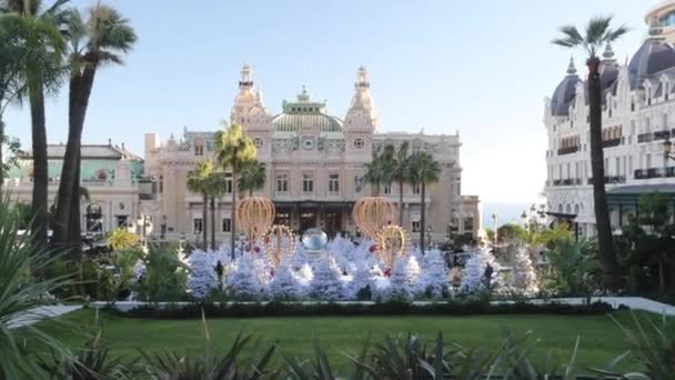 Monaco, Monte-Carlo, 25 December 2019: Panoráma a tér Kaszinó Monte-Carlo naplementekor, fehér karácsonyfák, hotel a Párizs, napos nap, karácsonyi dekoráció, turisták, szökőkút, új apartmanok — Stock videók