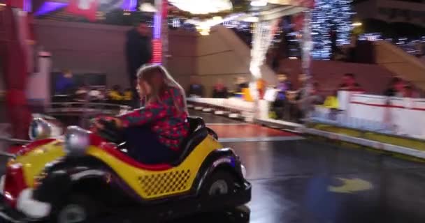 Monaco, Monte Carlo, 25. desember 2019: Barn rir på en attraksjon om kvelden, rir på maskiner og krasjer, ler muntert, lyser opp festlig, kaldt vær – stockvideo