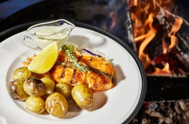 Izgara balık beyaz tabakta patates, limon ve sos, çıplak ateş, kırmızı kömür, duman, yakacak odun, 