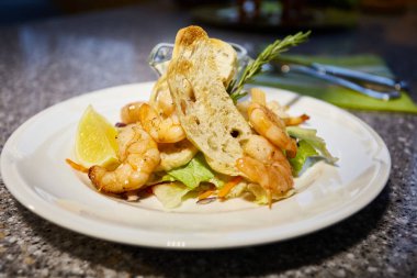 Izgara karides beyaz tabakta, tost, limon ve sos, kekik dalı, salata yaprağı.