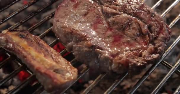 Il gran pezzo succoso di carne di manzo frigge su una griglia, il sangue emana, capovolge un pezzo su altro partito, un fumo e un vapore, una legna da ardere, mani della carne d'esposizione di chef, vicino — Video Stock